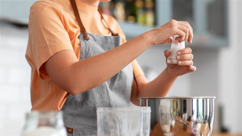 Woman adding salt to mixing bowl 