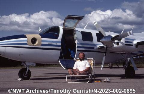  Tim Garrish sits on a lawn chair in front of a Conair Piper Aerostar in Yellowknife in 1983.  (NWT Archives/Timothy Garrish fonds/N-2023-002: 0895 - image credit)