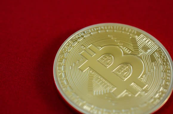 A physical gold bitcoin on a red background.