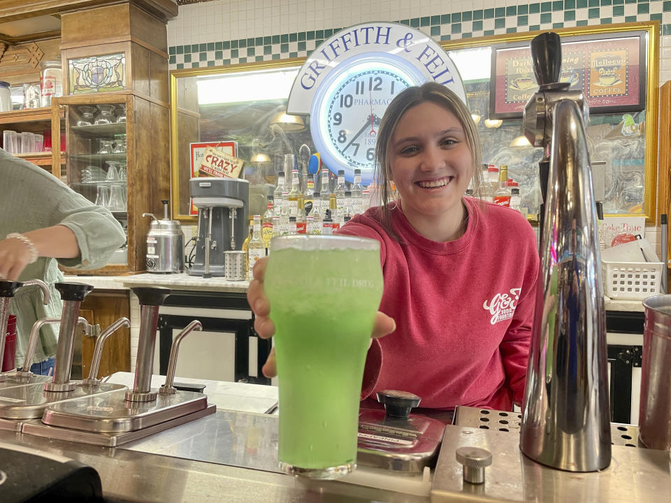 Malli Jarrett serves up an old-fashioned phosphate drink from the soda fountain at Griffith & Feil Drug on Thursday, March 30, 2023, in Kenova, W. Va. Soda fountains were often in pharmacies because pharmacists mixed tonics meant to heal ailments. Now they're preserving a style of living and an attitude that was common in little towns across America. (AP Photo/John Raby)