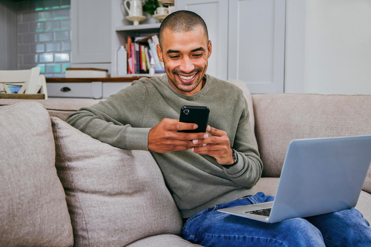 Man smiling while using his phone with his laptop on his lap