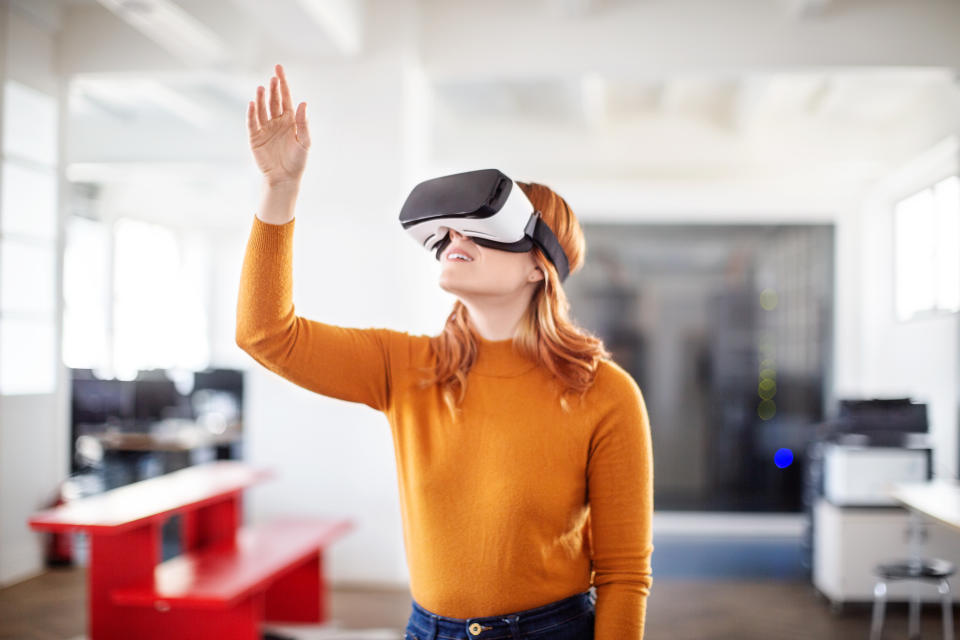 Curious young businesswoman using VR goggles and gesturing. Female executive using virtual reality glasses in office.