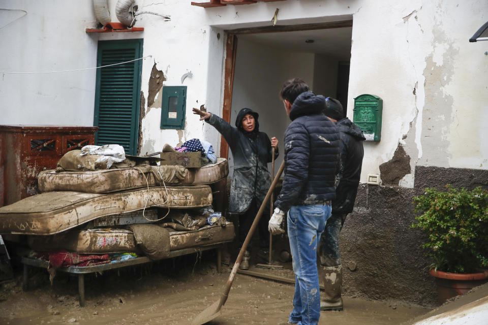 People remove mud from a house after heavy rainfall triggered landslides that collapsed buildings and left as many as 12 people missing, in Casamicciola, on the southern Italian island of Ischia, Saturday, Nov. 26, 2022. Firefighters are working on rescue efforts as reinforcements are being sent from nearby Naples, but are encountering difficulties in reaching the island either by motorboat or helicopter due to the weather. (AP Photo/Salvatore Laporta)