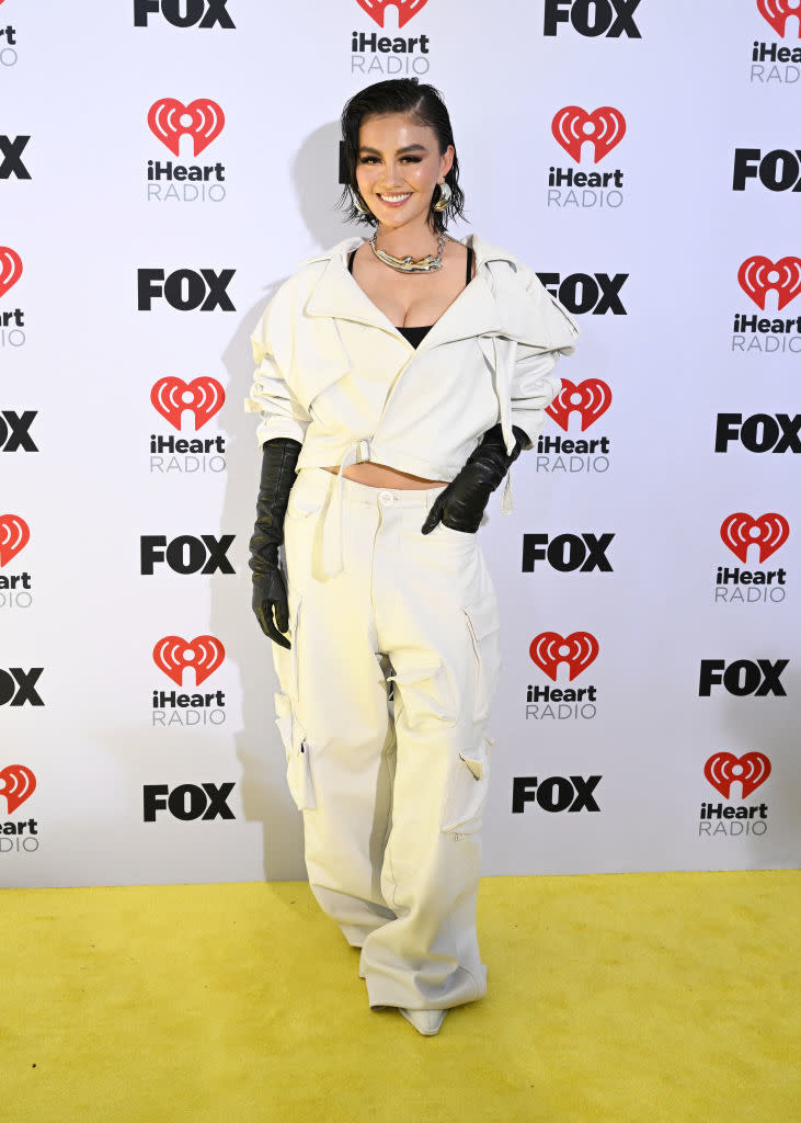 Person posing on the red carpet in an oversized white jacket and pants, accessorized with a necklace and gloves
