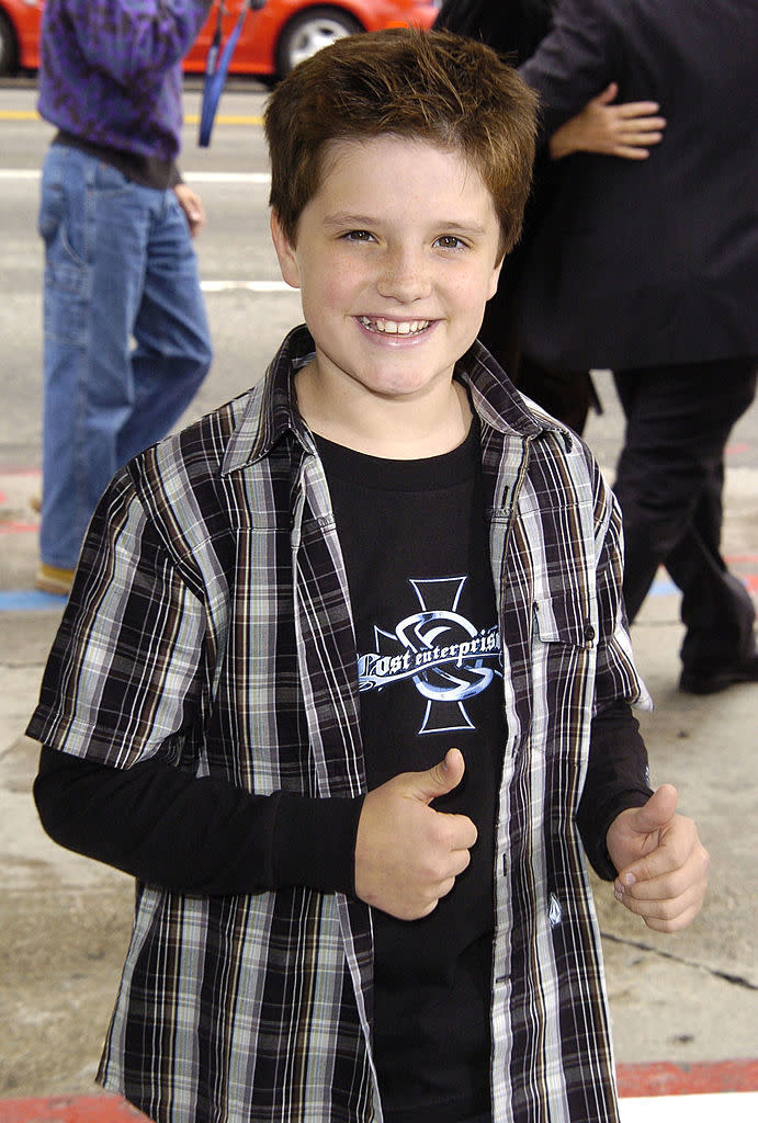 wearing a button-down over a long-sleeved shirt and short hair spiked in the front