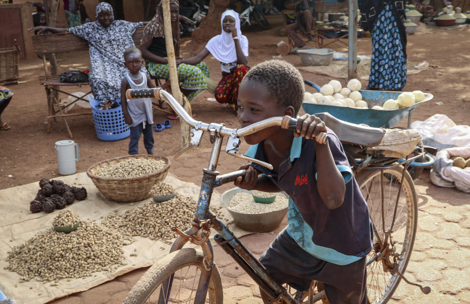 In this May 13, 2020, photo, a boy pushes his bicycle past food stalls at a market in Tougan, Burkina Faso. Violence linked to Islamic extremists has spread to Burkina Faso's breadbasket region, pushing thousands of people toward hunger and threatening to cut off food aid for millions more. (AP Photo/Sam Mednick)