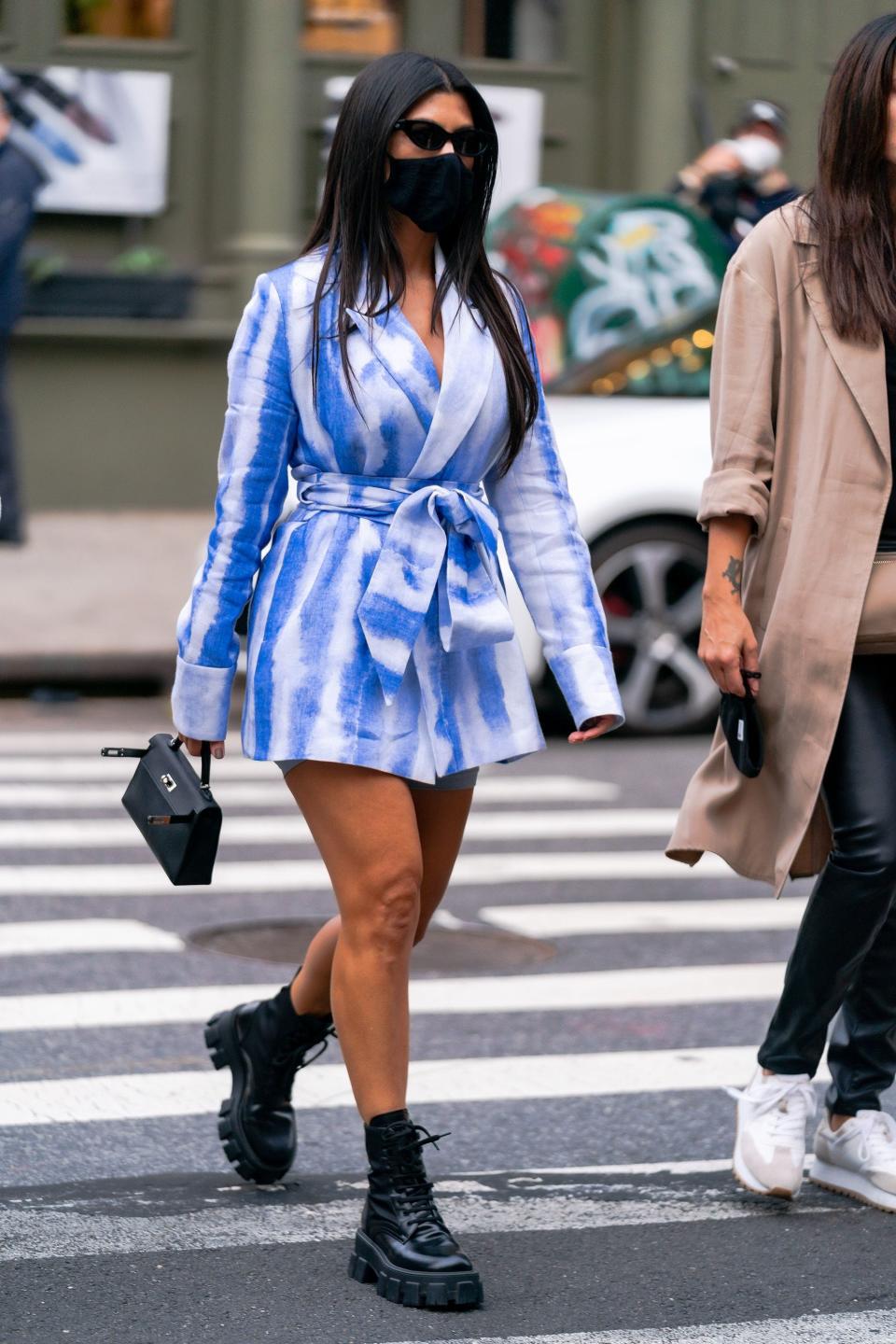Kourtney in a light blue tie dye belted blazer worn as a dress with a black face mask and combat boots.