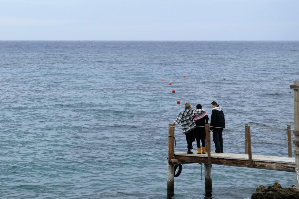 Nadine Kalache Maalouf, center, Celine Elbacha and Elbacha's daughter Morgane, right, stand on a deck at the seaside in eastern coastal resort of Paralimni, Cyprus, Wednesday, Dec. 22, 2021. They are among the thousands of Lebanese, including teachers, doctors and nurses who have left the country amid a devastating economic crisis that has thrown two thirds of the country’s population into poverty since October 2019. (AP Photo/Petros Karadjias)