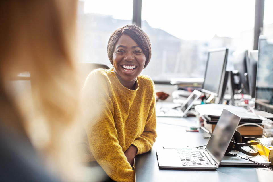 Two young business women working together in office, Female professionals sitting at the desk talking with each other and smiling.