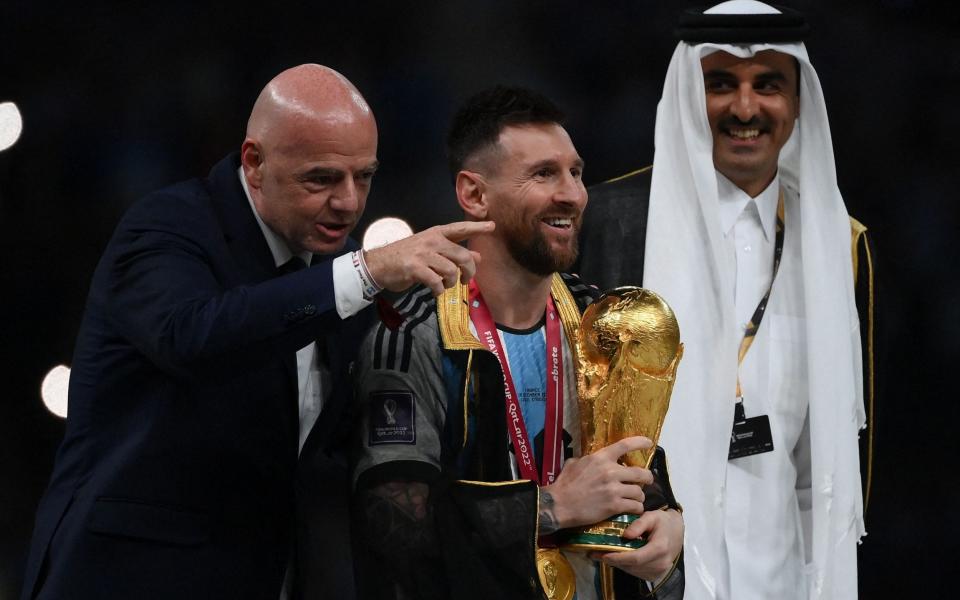 Fifa president Gianni Infantino looks on as a robed Messi prepares to lift the trophy in front of millions watching around the world - AFP/FRANCK FIFE