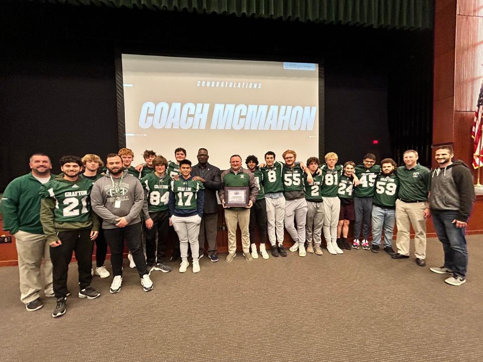 Grafton football players and staff surround coach Chris McMahon and New England Patriots legend Andre Tippett after the Patriots honored McMahon as their Coach of the Week.