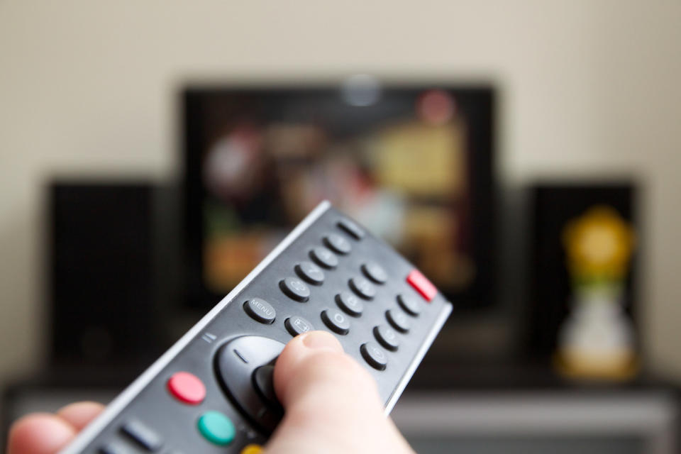 A person holding a remote control in front of a TV
