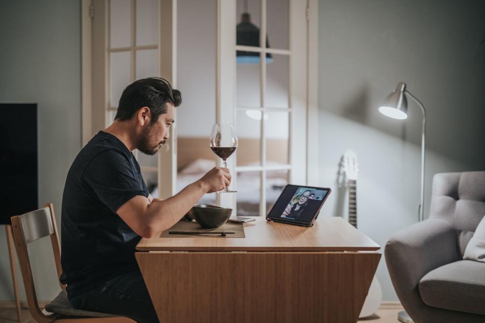 a man eating dinner in front of a laptop with a glass of red wine