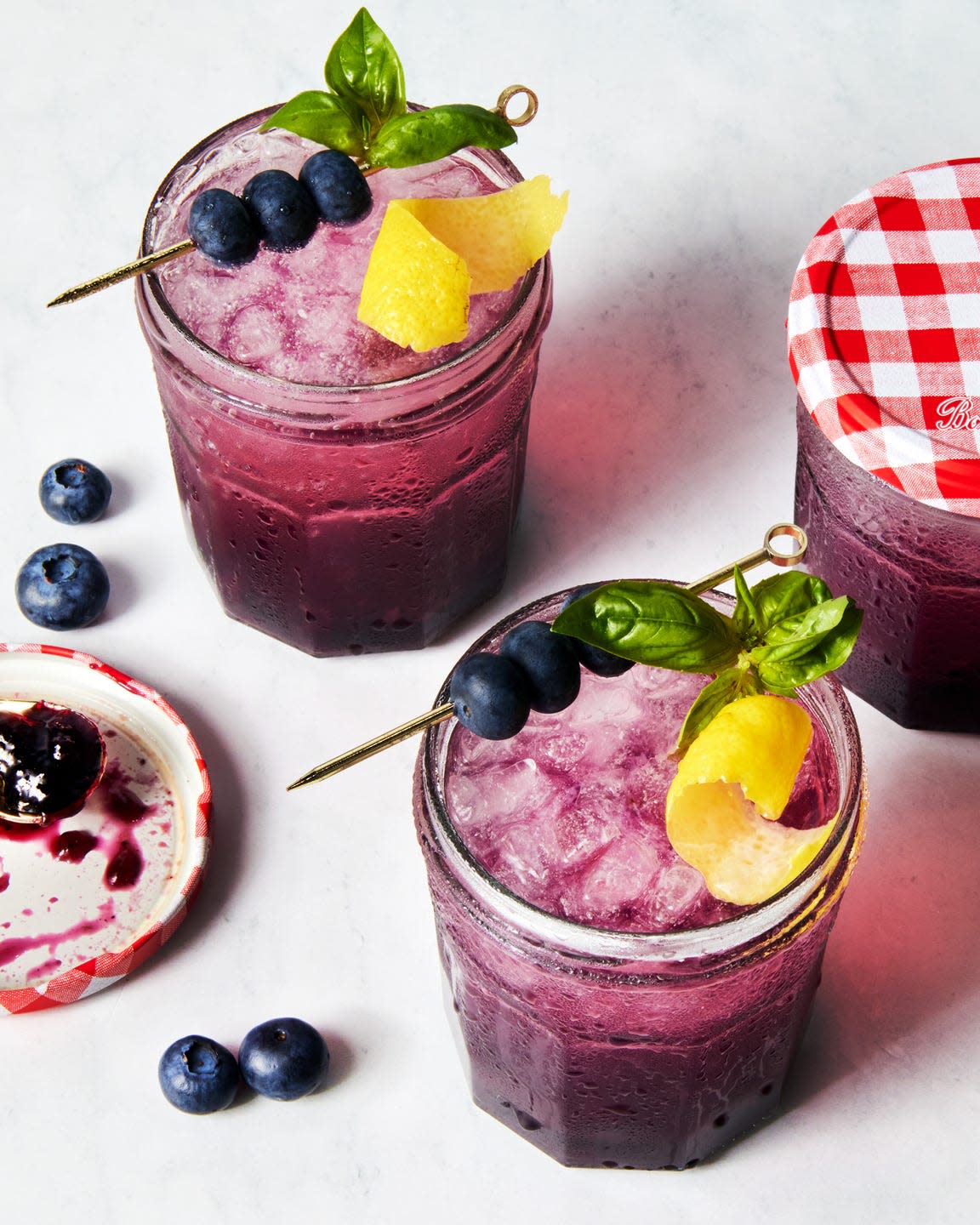 gin spritz in a jam jar garnished with a lemon twist and blueberries