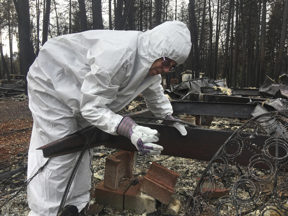 Joyce McLean, wearing a hazmat suit, looks through the remains of her home Wednesday, Dec. 5, 2018, in Paradise Calif. Some residents of a California town devastated by a catastrophic wildfire nearly a month ago were finally allowed to return home to sift through the charred remains in search of precious family heirlooms, photos and other possessions. A long line of cars waited in a cold drizzle at a checkpoint on their way to neighborhoods on the east side of Paradise. (AP Photo/Don Thompson)