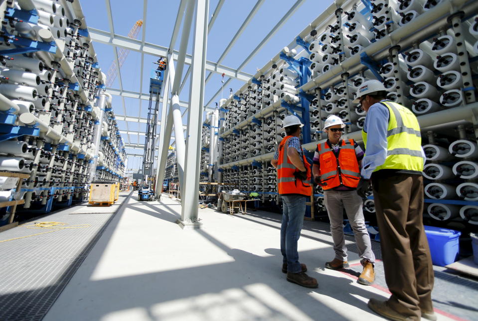 Poseidon Water project manager Peter MacLaggen (R) talks to fellow workers as they stand between rows of reverse osmosis filters at the Western Hemisphere's largest seawater desalination plant under construction in Carlsbad, California, April 14, 2015. Desalination has emerged as a newly promising technology in California in the face of a record dry spell that has forced tough new conservation measures, depleted reservoirs and raised the costs of importing fresh water from elsewhere. The biggest ocean desalination plant in the Western Hemisphere, a $1 billion project under construction since 2012 on a coastal lagoon in the California city of Carlsbad, is nearly completed and due to open in November, delivering up to 50 million gallons of water a day to San Diego County. To match Feature USA-DESALINATION/CALIFORNIA REUTERS/Mike Blake