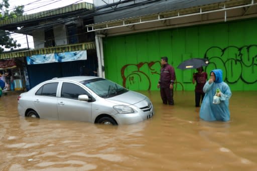 People walk past a car stuck in floodwaters in Jakarta