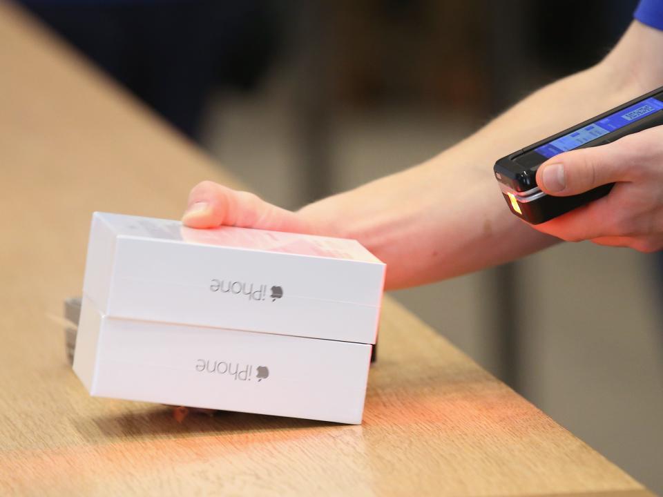 Close up of an Apple Store employee's hands holding two new iPhone boxes and scanning them with a special handheld sales device.