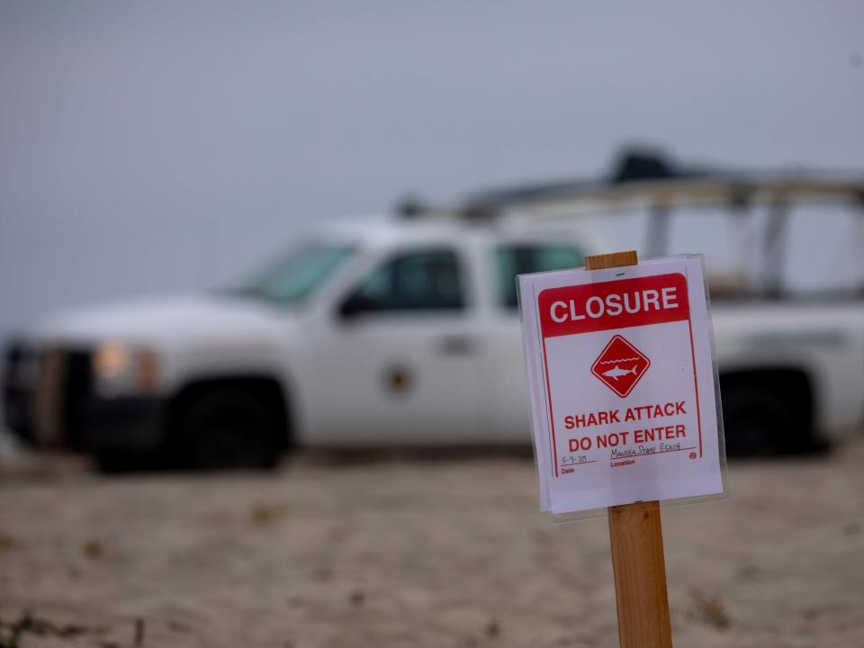 A lifeguard drives past a closure sign that says "Shark Attack, Do not enter."