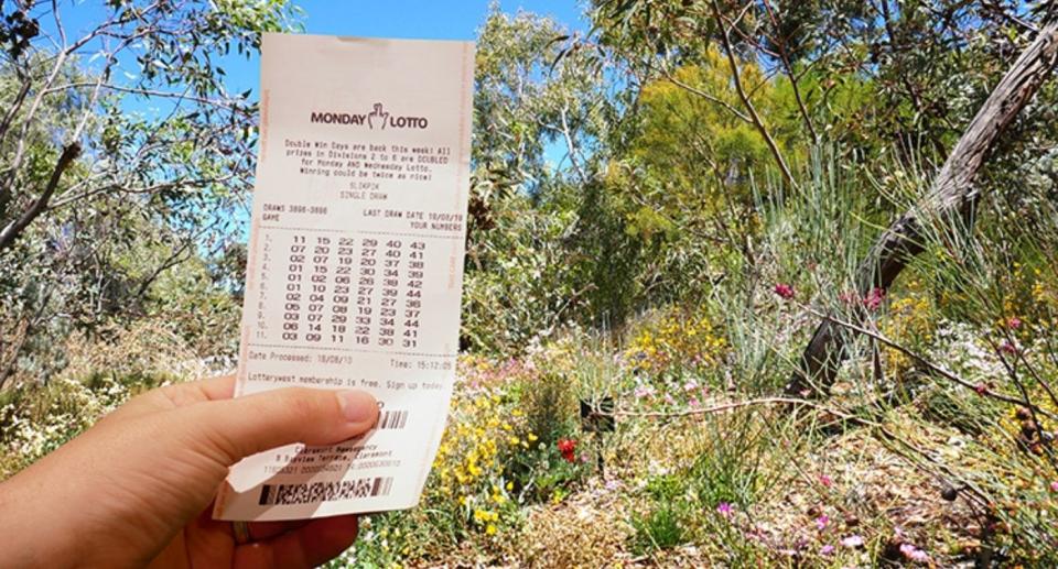Hand holds up lotto ticket in Aussie bush. Source: Lotterywest