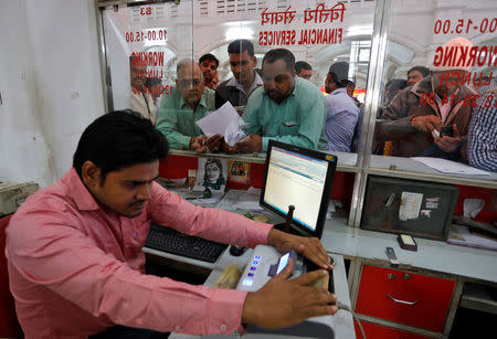 A cashier uses a machine to count 500 Indian rupee banknotes as customers wait in queues inside a post office in Lucknow, November 10, 2016. REUTERS/Pawan Kumar