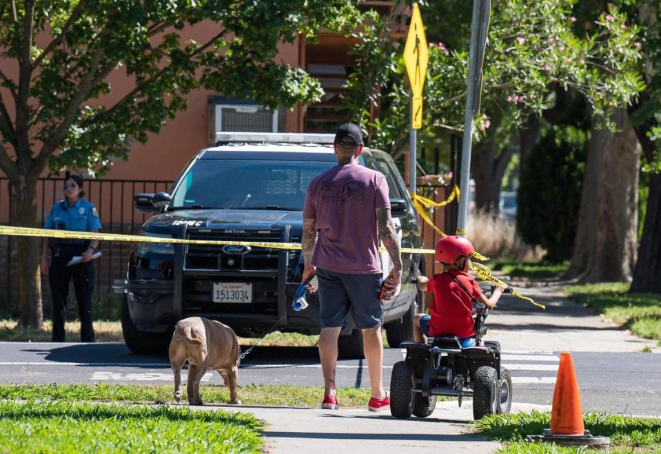 A family prepares to cross Q Street from Winn Park, past a scene where Sacramento police work Saturday, May 20, 2023, following an officer-involved shooting in midtown.
