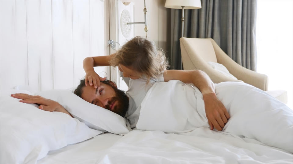 Little cute daughter comes to sleeping father at morning, and opens his eyes by fingers for wakes him. Family at home concept.