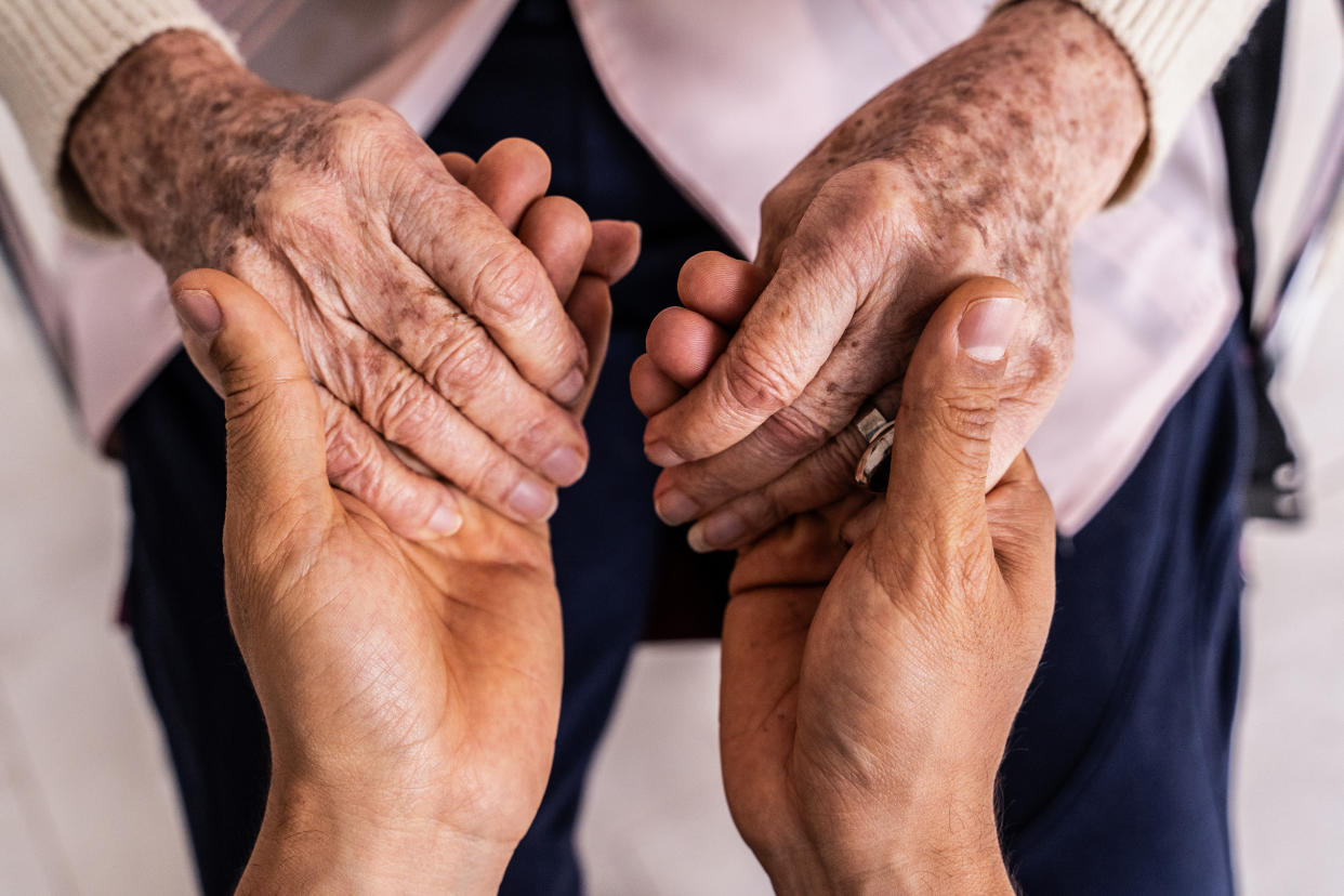 Close-up of a caregiver's hands holding the hands of a senior woman patient