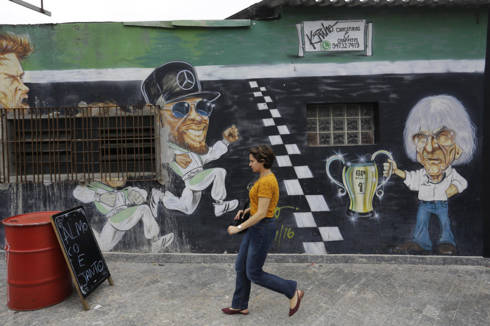 In this Nov. 7, 2019 photo, a mural depicts former F1 CEO Bernie Ecclestone, right, next to the world champion driver Lewis Hamilton, center, on the wall of a restaurant located in front of the Interlagos racetrack in Sao Paulo, Brazil. The metropolis' tourism agency says the F1 GP brought revenues of $80 million to Sao Paulo last year. (AP Photo/Nelson Antoine)