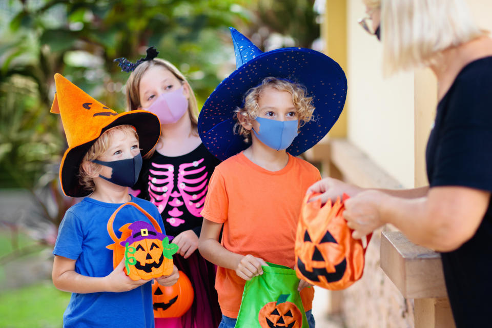 Kids trick or treat in Halloween costume and face mask. Children in dress up with candy bucket in coronavirus pandemic. Little boy and girl trick or treating with pumpkin lantern. Autumn holiday fun.