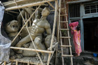 A woman hangs clothes outside her house, beside an unfinished idol of Hindu goddess Durga ahead of Durga Puja festival at Kumortuli, the potters' place, in Kolkata, India, Sunday, Sept. 18, 2022. The five-day festival commemorates the slaying of a demon king by goddess Durga, marking the triumph of good over evil. (AP Photo/Bikas Das)