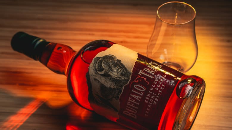 A bottle of Buffalo Trace whiskey next to an empty glass