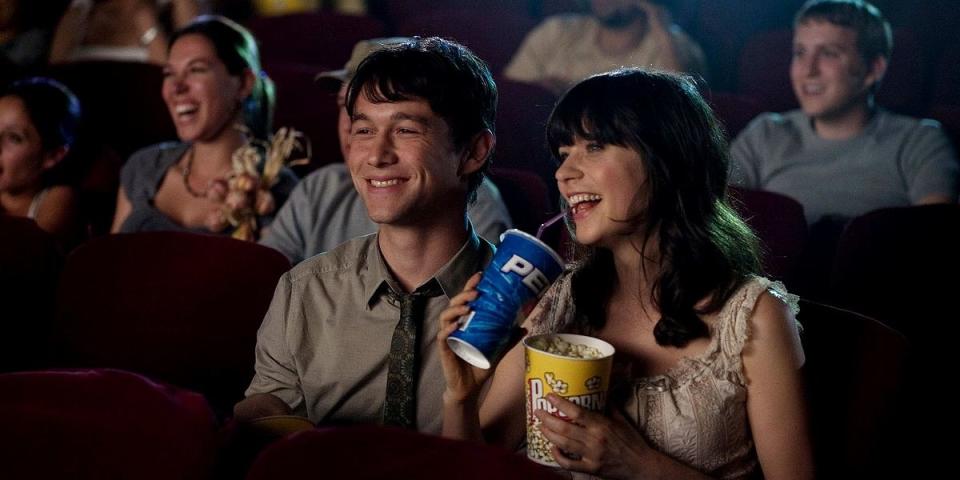 A couple watching a movie with a soda and popcorn in hand.