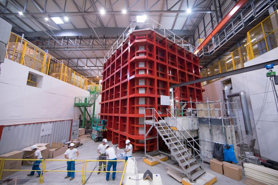 A large red container in a warehouse with workers in hardhats near it