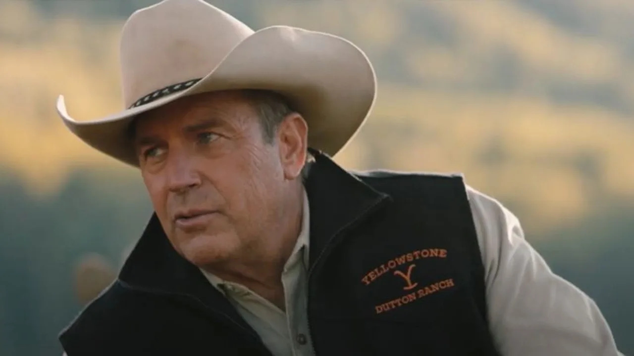  Kevin Costner as John Dutton wearing a cowboy hat and a Yellowstone vest, leaning to his left. 