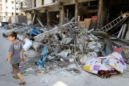 A boy walks past damaged shops in the rebel held Tariq al-Bab neighborhood of Aleppo, Syria, August 22, 2016. REUTERS/Abdalrhman Ismail