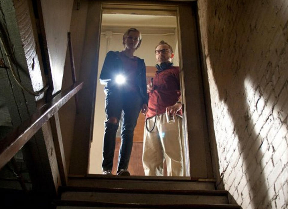 Sara Paxton and Pat Healy raise a flashlight at a darkened staircase while ghost hunting in "The Innkeepers"