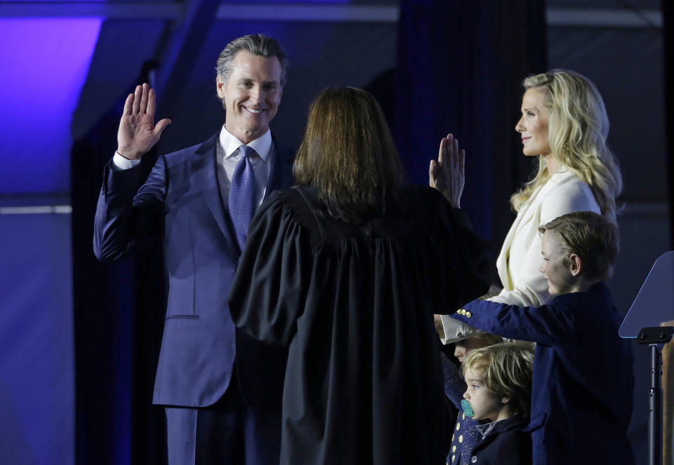 FILE - In this Jan. 7, 2019, file photo, California Governor Gavin Newsom takes the oath of office from state Supreme Court Chief Justice Tani Gorre Cantil-Sakauye during his inauguration in Sacramento, Calif. Looking on is Newsom's wife, Jennifer Siebel Newsom and their sons, Dutch, second from right, and Hunter, right. Newly elected California Gov. Gavin Newsom announced plans to expand Medicaid to those in the country illegally up to age 26 and implement a mandate that everyone buy insurance or face a fine. (AP Photo/Rich Pedroncelli, File)
