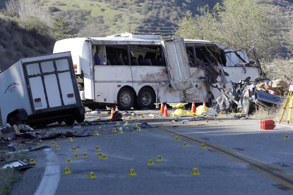 FILE - In this Feb. 4, 2013, file photo, evidence markers dot the road in front of the wreckage of a tour bus that crashed on Feb. 3, in the Southern California mountains near San Bernardino. Federal accident investigators called on Nov. 7, 2013, for a probe of the government agency charged with ensuring the safety of commercial vehicles, saying their own look into four tour bus, including the one on Feb. 3, and truck crashes that killed 25 people raises "serious questions" about how well the agency is doing its job. Federal inspectors gave the California tour bus company safety clearance a month before the accident. Seven passengers and a pickup truck driver were killed, 11 passengers were seriously injured and 22 others received minor to moderate injuries. The bus driver told passengers the bus’ brakes had failed. (AP Photo/Nick Ut, File)