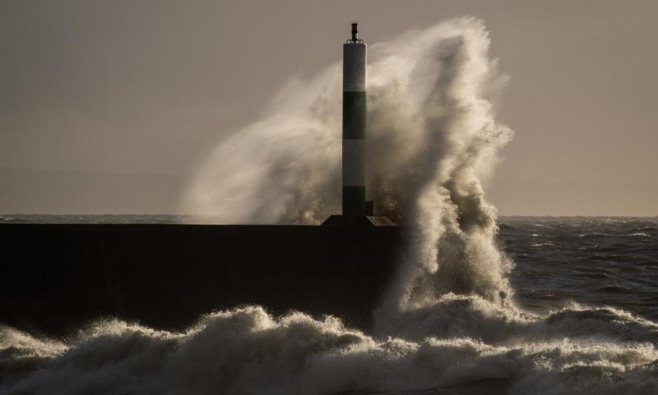 Waves batter the lighthouse and harbour wall in Aberystwyth, Wales