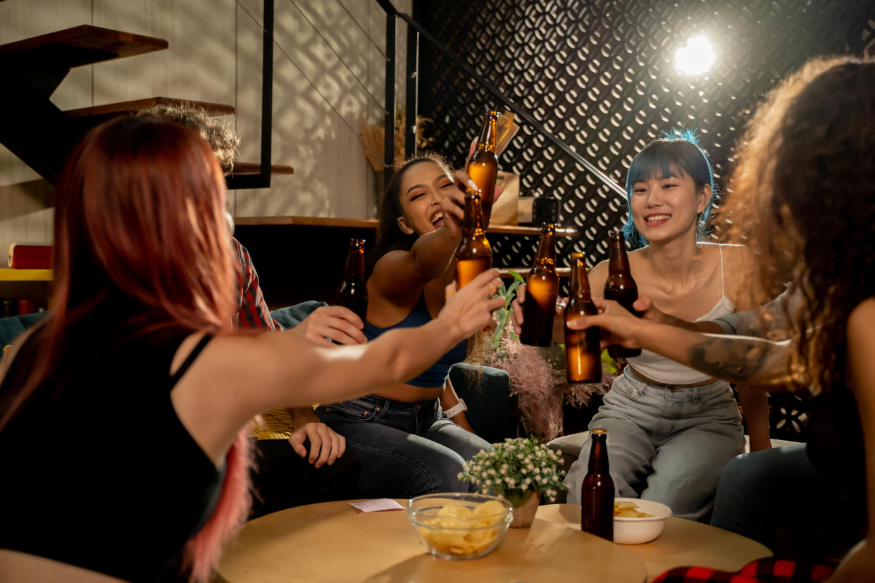 Diverse group of young people partying and toasting a drink in the house enjoying nightlife. Multiethnic friendship and social gathering concept.