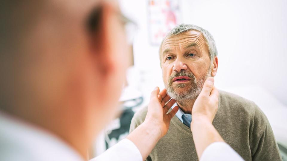 Over the shoulder view of a doctor touching a patientâ€™s throat while doing a medical exam.