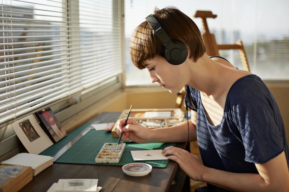 A woman listens to music on headphones while painting