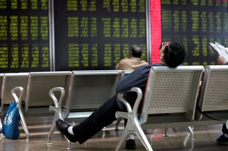 An investor takes a nap in front of a board showing stock information in Beijing