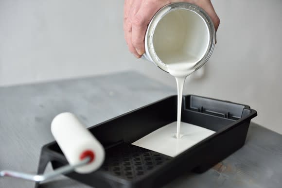 A hand pouring white paint into a pan with a roller next to it