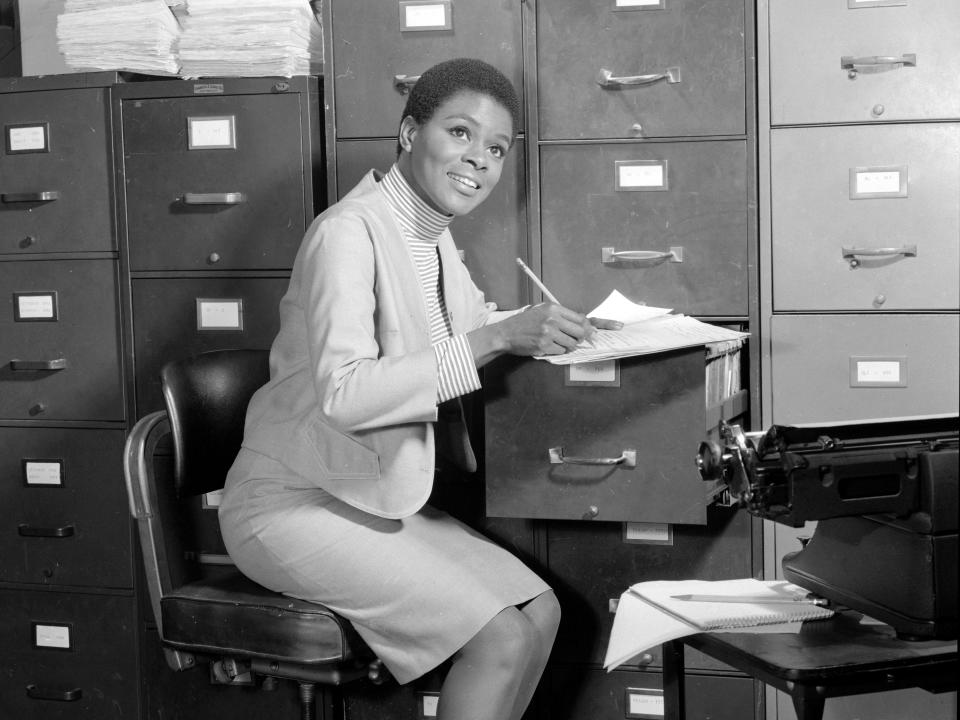 Black and white photo of Cicely writing on papers on a filing cabinet.