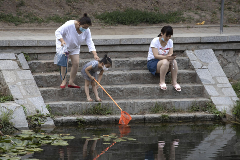 A woman holds on to the shirt of a chid using a net to look for fish as they wear masks to curb the spread of the coronavirus along a canal in Beijing on Saturday, June 20, 2020. China's capital recorded a further drop in coronavirus cases amid tightened containment measures. (AP Photo/Ng Han Guan)