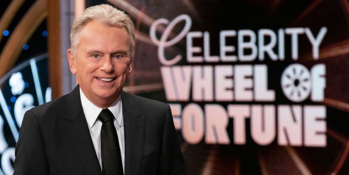 pat sajak smiling for a photo in front of the wheel of fortune logo