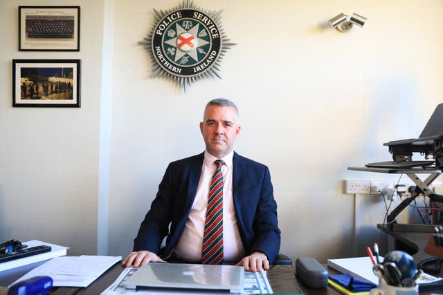 Liam Kelly sitting behind a desk, with the PSNI logo on the wall behind him