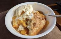Peach cobbler in a bowl with a scoop of vanilla ice cream, with a spoon